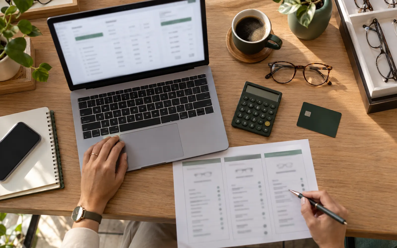 Mesa com notebook, calculadora e cartão comparando a mensalidade de sistemas para ótica.